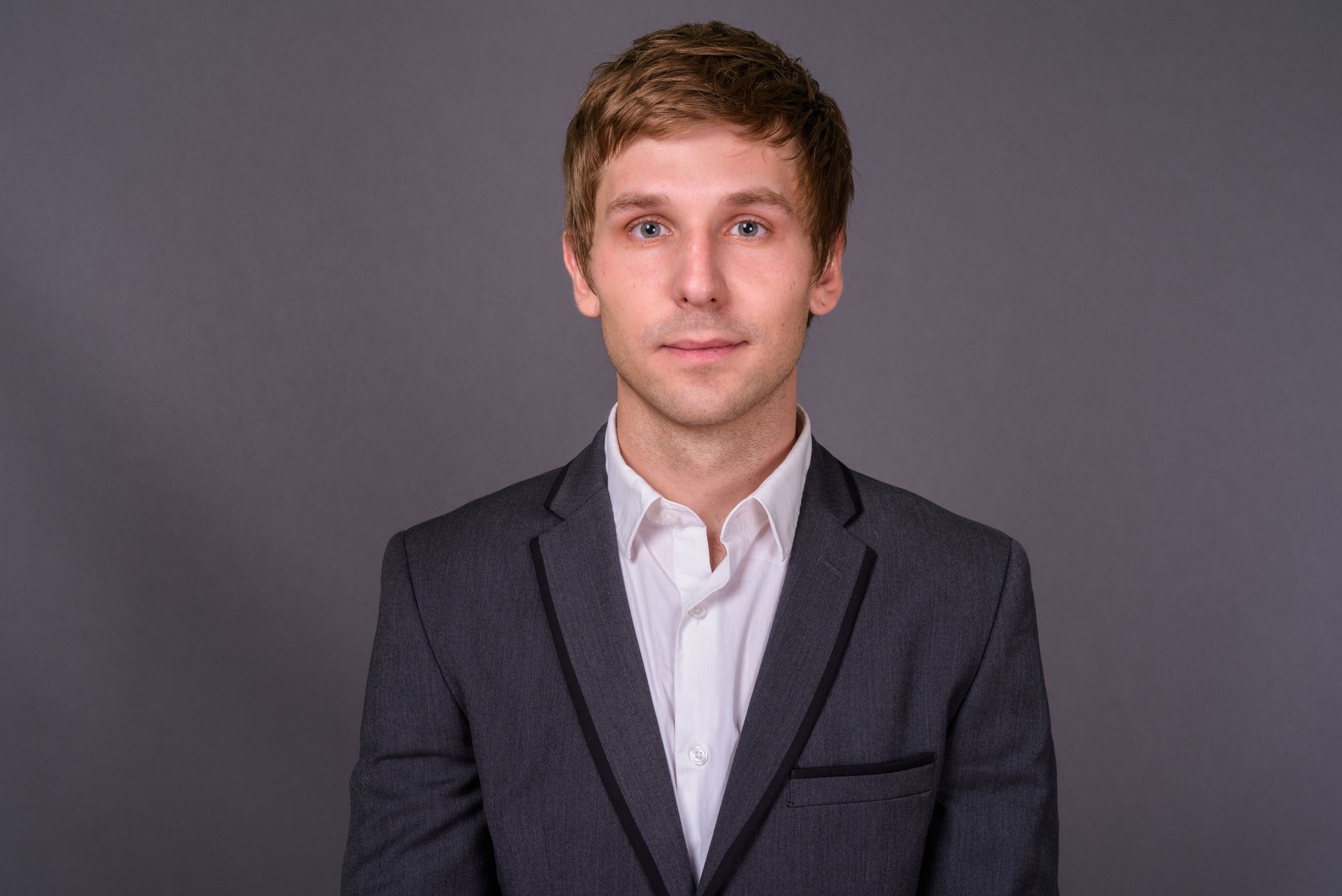 Young handsome businessman wearing suit against gray background
